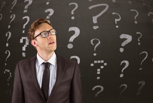 A business person thinking Infront of a black board with question marks